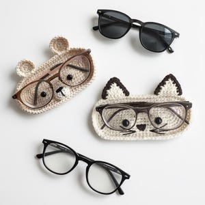 Puede incluir: Una variedad de gafas y gafas de sol, incluyendo dos pares de gafas con montura negra y un par de gafas de sol con lentes oscuras. También hay dos estuches de ganchillo para gafas con forma de oso y gato.