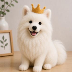 Op de afbeelding: Een naaldgevilte witte hondenfiguur met pluizige vacht, zwarte ogen, een zwarte neus en een geopende bek met een roze tong. De hond draagt een kleine, getextureerde mosterdgele kroon die tussen de puntige oren is geplaatst.