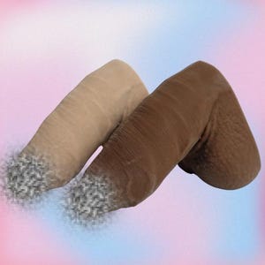 May include: Two prosthetic penises, one in a light beige and the other in a dark brown hue, are shown against a soft, gradient background. The tips of the penises have a textured, speckled appearance. The products are designed for medical or novelty purposes.