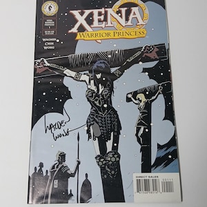 May include: A comic book cover for "Xena: Warrior Princess" features a stylized illustration of Xena on a cross. The cover has the title "XENA WARRIOR PRINCESS" and the names Wagner, Chin, and Wong. The comic is signed.