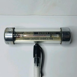 May include: A horizontal cylindrical food-safety indicator thermometer with chrome end caps. The glass face features the text "FREEZING ZONE (32) SAFETY ZONE (50) DANGER ZONE" and "FOOD-SAFETY INDICATOR" with a red liquid temperature gauge.