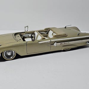 Könnte beinhalten: Goldfarbenes Cabrio-Automodell mit weißem Innenraum. Das Modell verfügt über detaillierte Chromakzente, Drahtspeichenräder und ein beiges Verdeck. Das Auto ist ein klassisches Vintage-Design, wahrscheinlich aus der Mitte des 20. Jahrhunderts.