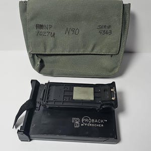 May include: An olive green canvas bag with the text "NP 1027U N90 SER# 4363" printed on it, and a black "PROBACK by FORSCHER" camera back. The camera back is rectangular with a black strap.
