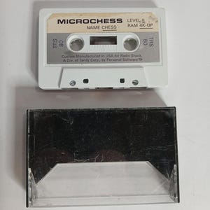 May include: A white Microchess cassette tape with the text "MICROCHESS LEVEL II" and "NAME CHESS". The cassette is labeled "TRS 80" and "RAM 4K-UP". The cassette case is clear and black.