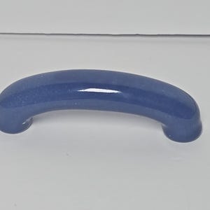 May include: A smooth, arched cabinet handle with a glossy, deep blue finish. The hardware features a curved, semi-circular design with rounded ends, providing a sleek and uniform appearance suitable for attachment to drawers or cabinet doors.