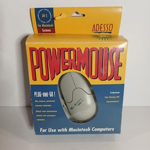May include: A vintage Adesso PowerMouse for Macintosh computers. The box is yellow and blue, with the word "POWERMOUSE" in large red letters. The mouse is light gray and has two buttons. The box states "Plug-and-Go!" and "2 Button For Power PC Compatibility."