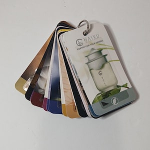 May include: A fan-shaped collection of rectangular cards held together by a metal ring. The top card features a graphic of a bottle with the text HAIKU POETRY FOR YOUR SENSES. Each card displays different colors and imagery, including gold, black, blue, and white tones.