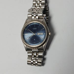 May include: A silver-toned Citizen Quartz watch with a blue dial and a date display showing "TUE 17." The watch has a fluted bezel and a linked metal band.