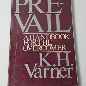 May include: A rectangular book with a deep maroon cover featuring the title PREVAIL in large light gray letters. Below the title, the text reads A HANDBOOK FOR THE OVERCOMER in smaller white letters, followed by the author name K.H. Varner in white.