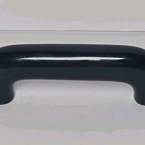 May include: A solid black cabinet handle with a smooth, glossy finish and a rounded, arch-shaped design. The handle features two vertical mounting points on either end, creating a simple, curved bridge shape that is uniform in thickness throughout.
