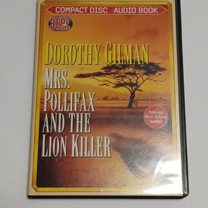 May include: A compact disc audio book titled "Dorothy Gilman Mrs. Pollifax and the Lion Killer." The cover features a desert landscape with a tree and the text "National Best Selling Author." The disc case is black with a gold and orange cover.