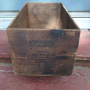 May include: A vintage wooden box with the text "Kingsbury Toys" and "Automatic Fire Station" printed on the front. The box is made of dark brown wood and has a rectangular shape.