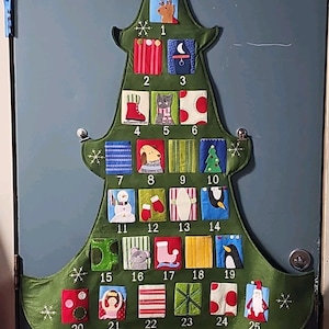 May include: A green fabric Christmas tree wall hanging featuring twenty-five numbered pockets. Each pocket displays a unique colorful applique design, including animals, holiday symbols, and patterns. A yellow fabric star sits at the top peak.