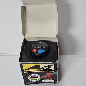 May include: A black Avenir cycle computer with a digital display and two buttons, one red and one blue, housed in its original cardboard box. The box features the Avenir logo, the text "cycle computer," and a "World Champion" emblem graphic.