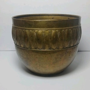 Peut inclure: Un bol de couleur bronze avec une base arrondie et une bande décorative ornée de motifs ovales et tourbillonnants. Le bol a une large ouverture et une finition lisse et polie, adaptée à un usage décoratif.