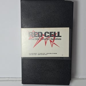 Può includere: Una custodia per videocassetta VHS nera con una copertina di carta bianca che riporta il testo RED CELL Secret SEAL Terrorist Operations in caratteri neri e rossi. La parte inferiore della copertina include i contatti di Paladin Press e l'ISBN 0-87364-766-1.