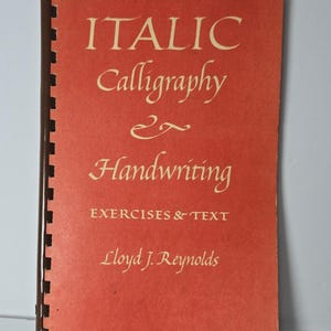 May include: A spiral-bound instructional book with a bright orange cover. The text on the cover reads: ITALIC Calligraphy & Handwriting EXERCISES & TEXT by Lloyd J. Reynolds. The binding is a dark brown plastic coil along the left side of the book.