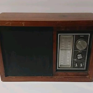 Puede incluir: Una radio de madera vintage con un acabado marrón oscuro. La radio presenta un panel de altavoz negro y un panel de control con un dial de sintonización, control de volumen e interruptor de encendido. La cara de la radio muestra números de frecuencia.