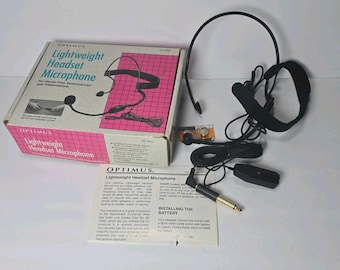 May include: An Optimus Lightweight Headset Microphone with a black adjustable headband, a boom microphone, a wired connection with a 1/4 inch plug, a small battery, and an instruction manual, all packaged in a box with pink and white grid graphics.