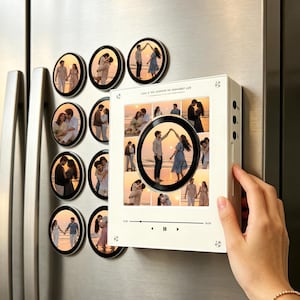 May include: A white rectangular music player frame featuring a central circular photo and a grid of smaller photos, accompanied by eight circular photo magnets. The frame displays text at the top and a digital playback interface at the bottom.
