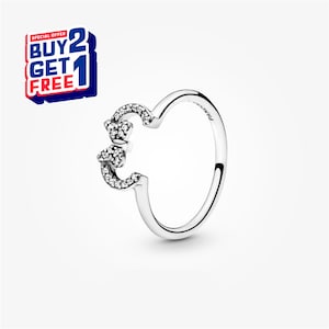 May include: A silver ring featuring a bow design, embellished with small, clear gemstones. The ring has a polished finish and a curved band. The image also includes a red, white, and blue graphic that says "BUY 2 GET 1 FREE".
