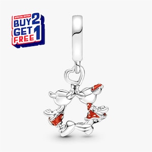 Puede incluir: Un charm de plata con una parte superior en forma de coraz&oacute;n y un dise&ntilde;o circular con personajes de dibujos animados con detalles en rojo. El charm tiene un dise&ntilde;o colgante y es probablemente un accesorio de joyer&iacute;a. La imagen tambi&eacute;n incluye una oferta promocional "COMPRA 2 Y LL&Eacute;VATE 1 GRATIS".