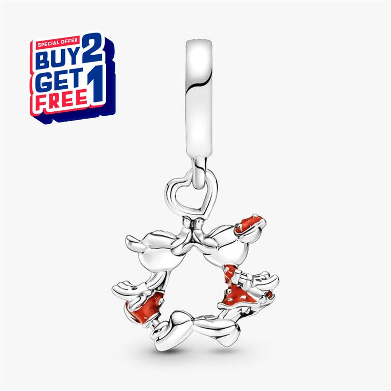 Puede incluir: Un charm de plata con una parte superior en forma de coraz&oacute;n y un dise&ntilde;o circular con personajes de dibujos animados con detalles en rojo. El charm tiene un dise&ntilde;o colgante y es probablemente un accesorio de joyer&iacute;a. La imagen tambi&eacute;n incluye una oferta promocional "COMPRA 2 Y LL&Eacute;VATE 1 GRATIS".