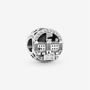 May include: A silver charm featuring a detailed depiction of a building, possibly a landmark, with a British flag. The charm is adorned with clear gemstones and the word "LONDON" is engraved on the side. The charm is round with a hole for a bracelet or necklace.