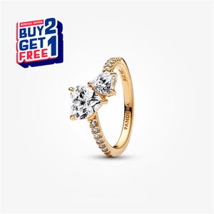 May include: A gold-colored ring with two clear, heart-shaped gemstones. The ring band is embellished with small, clear stones. The text "SPECIAL OFFER BUY 2 GET 1 FREE" is in a red, white, and blue banner.