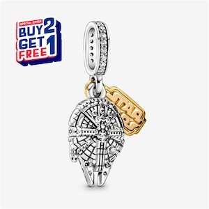 Könnte beinhalten: Ein silberner Charm-Anhänger mit dem Design des Millennium Falcon und einem goldfarbenen Star Wars Logo-Anhänger. Der Charm hat eine silberne Schlaufe mit klaren Steinen. Das Bild enthält auch ein "Kaufe 2, erhalte 1 gratis" Angebot.