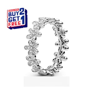 Puede incluir: Un anillo plateado con un diseño floral. Cada flor está adornada con pequeñas piedras preciosas transparentes. El anillo se muestra sobre un fondo blanco. Un gráfico promocional con el texto "BUY 2 GET 1 FREE" está en la esquina superior izquierda.