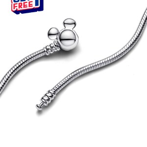 K&ouml;nnte beinhalten: Ein silbernes Armband mit einem Mickey-Mouse-f&ouml;rmigen Verschluss. Das Armband hat ein Schlangenketten-Design. Das Bild enth&auml;lt auch eine rot-wei&szlig;-blaue Grafik mit der Aufschrift "BUY 2 GET 1 FREE".