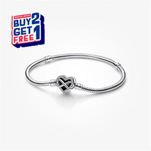 Könnte beinhalten: Ein silbernes Armband mit einem herzförmigen Anhänger mit einem Unendlichkeitssymbol. Der Anhänger ist mit kleinen, klaren Steinen besetzt. Das Armband hat ein Schlangenketten-Design. Das Bild enthält auch eine Werbegrafik "KAUFE 2 BEKOMME 1 GRATIS".