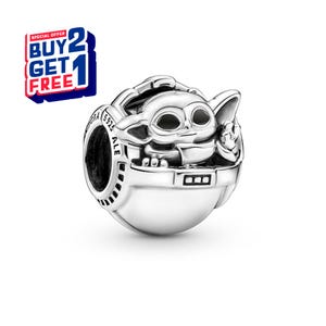 May include: A silver charm featuring a stylized depiction of Grogu, also known as Baby Yoda, from The Mandalorian. The charm is in a pod-like carrier, with the text "S925 ALE" visible. A "BUY 2 GET 1 FREE" offer is in the upper left corner.