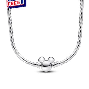 K&ouml;nnte beinhalten: Eine silberfarbene Halskette mit einem Mickey Mouse-Anh&auml;nger. Die Halskette hat ein Schlangenketten-Design und einen runden Anh&auml;nger mit zwei kleinen Kreisen oben und einem gr&ouml;&szlig;eren Kreis darunter. Das Bild enth&auml;lt auch ein "KAUFE 2 BEKOMME 1 GRATIS"-Angebot.