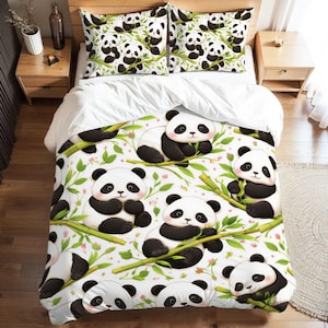 May include: A white duvet cover and two pillowcases featuring a panda bear design. The pandas are black and white, with pink cheeks, and are surrounded by bamboo and green leaves. The bedding set is on a wooden bed frame.