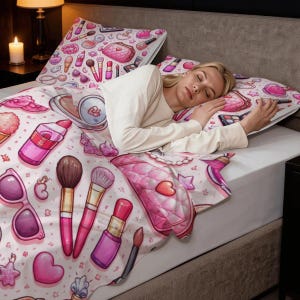 Op de afbeelding: Een beddengoedset met een roze en wit make-up thema. De set bevat een dekbedovertrek en kussenslopen versierd met illustraties van lippenstift, make-up borstels, handtassen en zonnebrillen. Het beddengoed heeft een cartoonstijl.