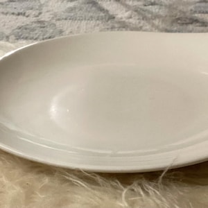 May include: A white, leaf-shaped serving dish. The dish has a smooth, glossy finish and a slightly raised edge. The design includes a small, curved handle on one end. This dish is suitable for serving appetizers or small portions.