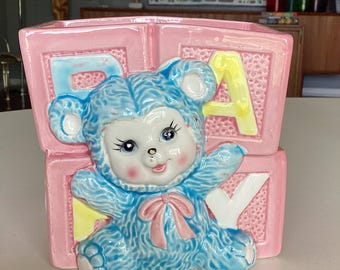Decoración infantil vintage: maceta con forma de oso azul antropomórfico y bloques de alfabeto rosas.
