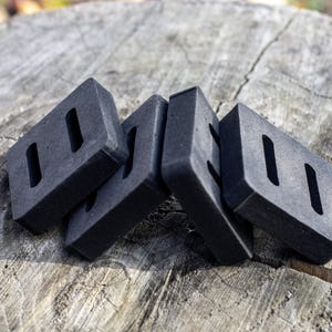 May include: Four dark gray rectangular objects with two rectangular cutouts each, arranged on a weathered wooden surface. The objects appear to be made of a dense material.