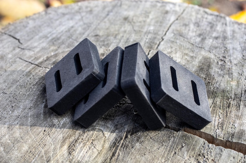 May include: Four dark gray rectangular objects with two rectangular cutouts each, arranged on a weathered wooden surface. The objects appear to be made of a dense material.