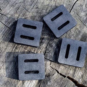 May include: Four gray, square foam pads with two rectangular cutouts each, arranged on a weathered, gray tree stump. The pads are evenly spaced and appear to be new.