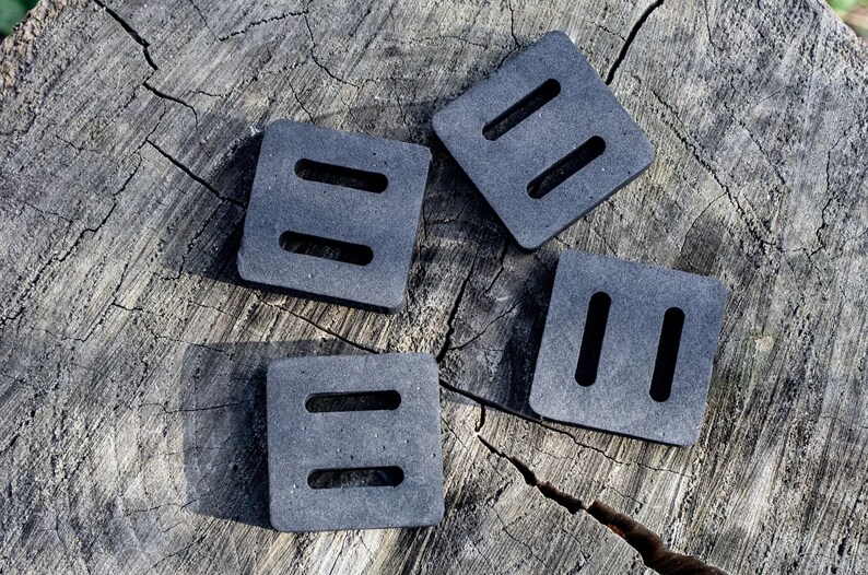 May include: Four gray, square foam pads with two rectangular cutouts each, arranged on a weathered, gray tree stump. The pads are evenly spaced and appear to be new.