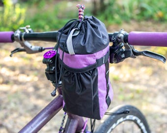 Bolsa de manillar Bikepacking Feed Bag - Color lila, ideal para ciclismo y gravel touring. Ligera y de fácil acceso. Material X-Pac.