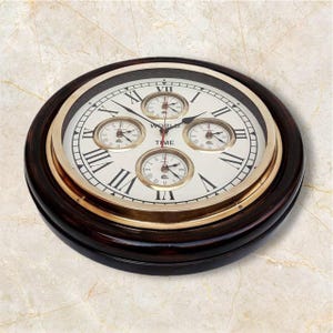 May include: A round wall clock with a dark brown wooden frame and a gold-toned metal bezel. The off-white face features large black Roman numerals, the word WORLD TIME, and four smaller circular sub-dials with black hands and markings.