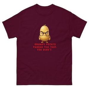 May include: Burgundy t-shirt with a cartoon potato wearing glasses and looking cross. The text says "GRUMPY POTATO PASSED THE TEST. YOU DIDN'T." A fun design for everyday wear.