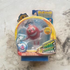 May include: A Pac-Man and the Ghostly Adventures Pac's Pal Spiral toy figure in a clear plastic package. The red figure has a smiling face and is labeled as a Pac Spinner toy.