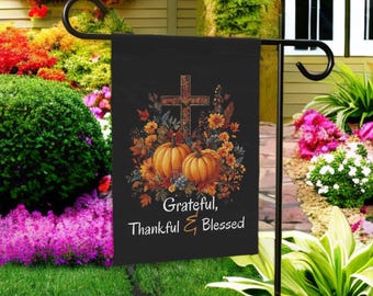 May include: Black garden flag featuring a cross, pumpkins, and fall foliage in shades of orange, yellow, and brown. The flag reads "Grateful, Thankful & Blessed". The flag is displayed on a black metal stand in a garden setting.