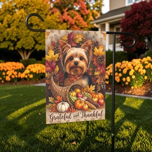 Puede incluir: Una bandera de jardín rectangular con un Yorkshire Terrier que lleva un pañuelo de cuadros rojos, rodeado de hojas de otoño, piñas y un cuerno de la abundancia lleno de calabazas, manzanas y maíz. El texto Grateful and Thankful está abajo.