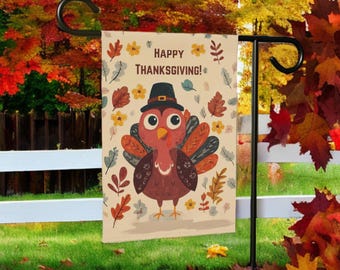 Può includere: Una bandiera da giardino del Ringraziamento con un tacchino dei cartoni animati con un cappello da pellegrino, circondato da foglie d'autunno e fiori. La bandiera recita "HAPPY THANKSGIVING!" in un carattere decorativo. La bandiera è esposta su un supporto di metallo nero in un giardino.